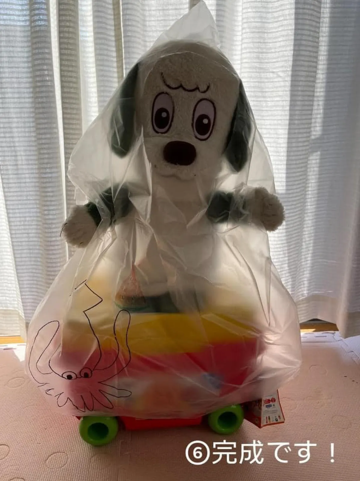 イカの絵を描いた完成品のゴミ袋を、犬のぬいぐるみが着ている。