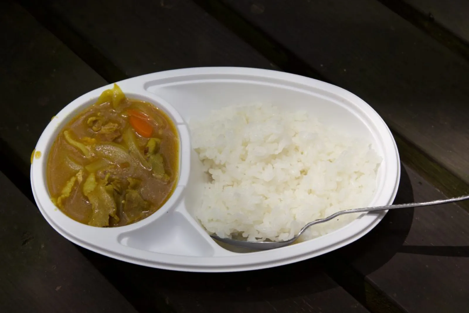 野外炊事で作ったカレーライス。白い仕切り皿にごはんとカレーが盛られ、スプーンが添えてある。