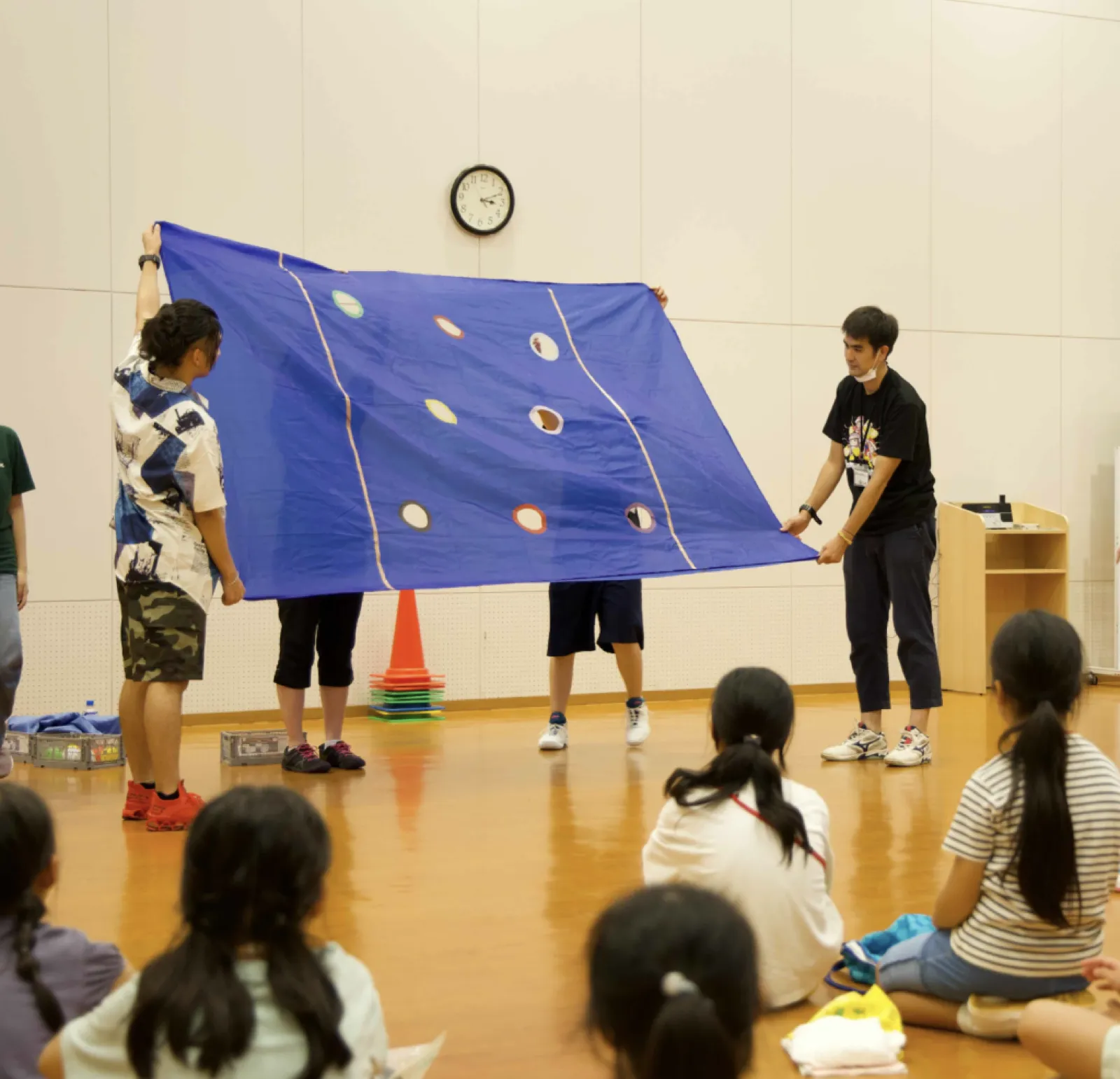 運動会のゲームで、スタッフが丸い穴の開いた大きな青い布を広げている。