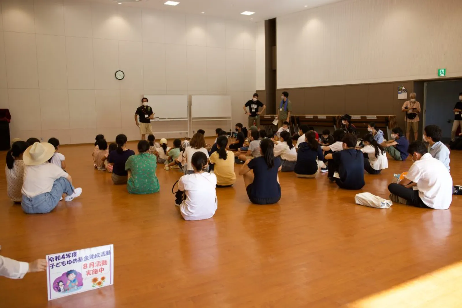 運動会の前、体育館の床に座った子どもたちが、前に立つスタッフの話を聞いている。