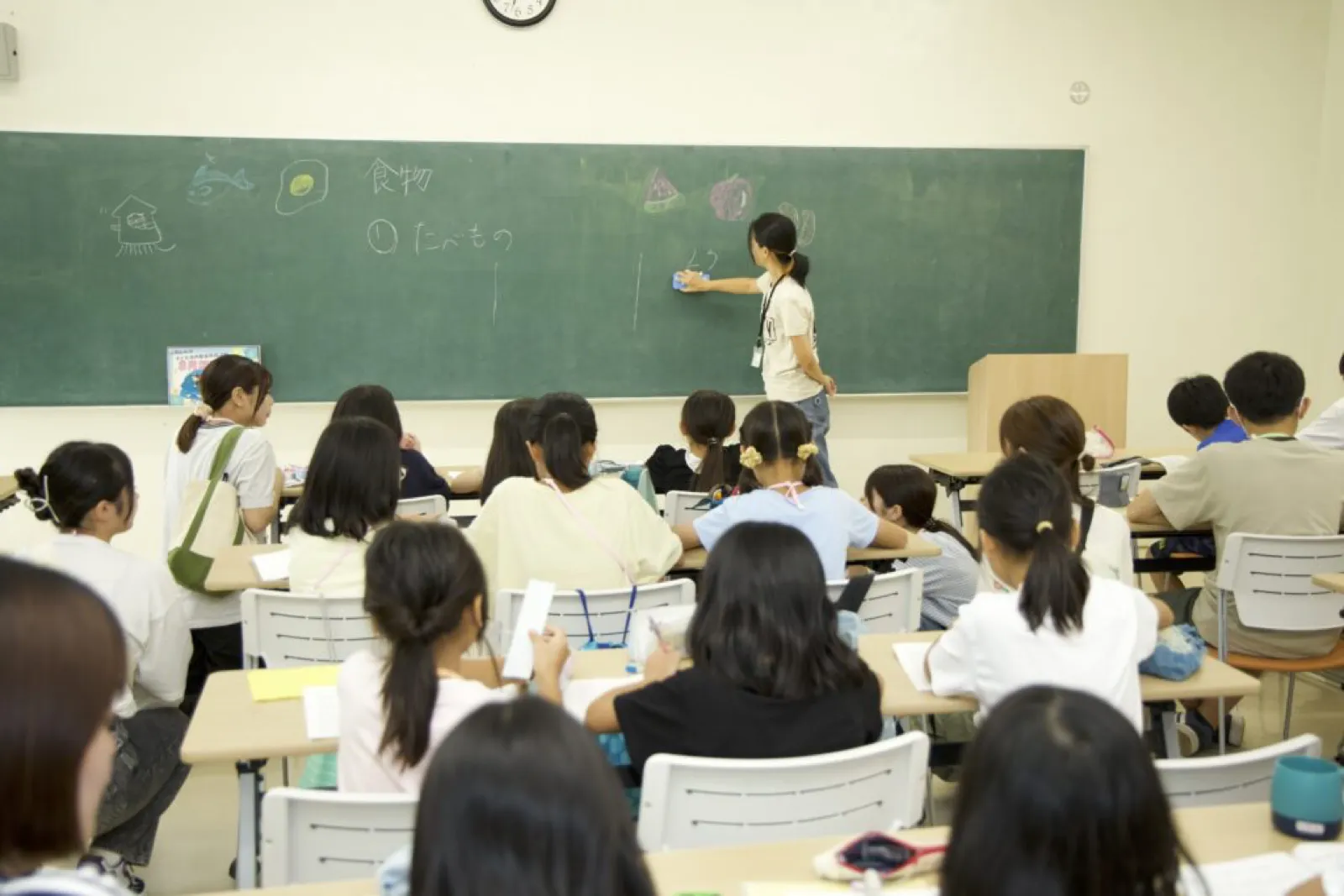 学習会で、黒板に食べ物の絵を描いて説明するスタッフと、話を聞く子どもたち。