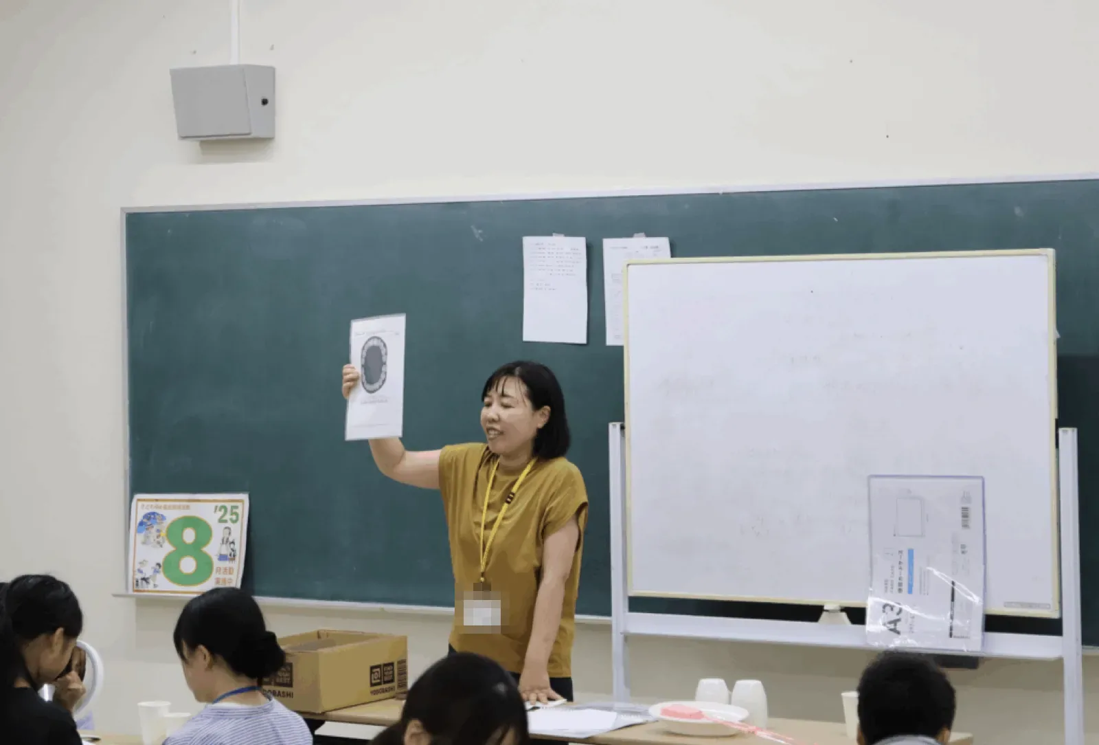 歯磨きの学習会で、スタッフが歯の絵を印刷した紙を高く掲げて説明している。