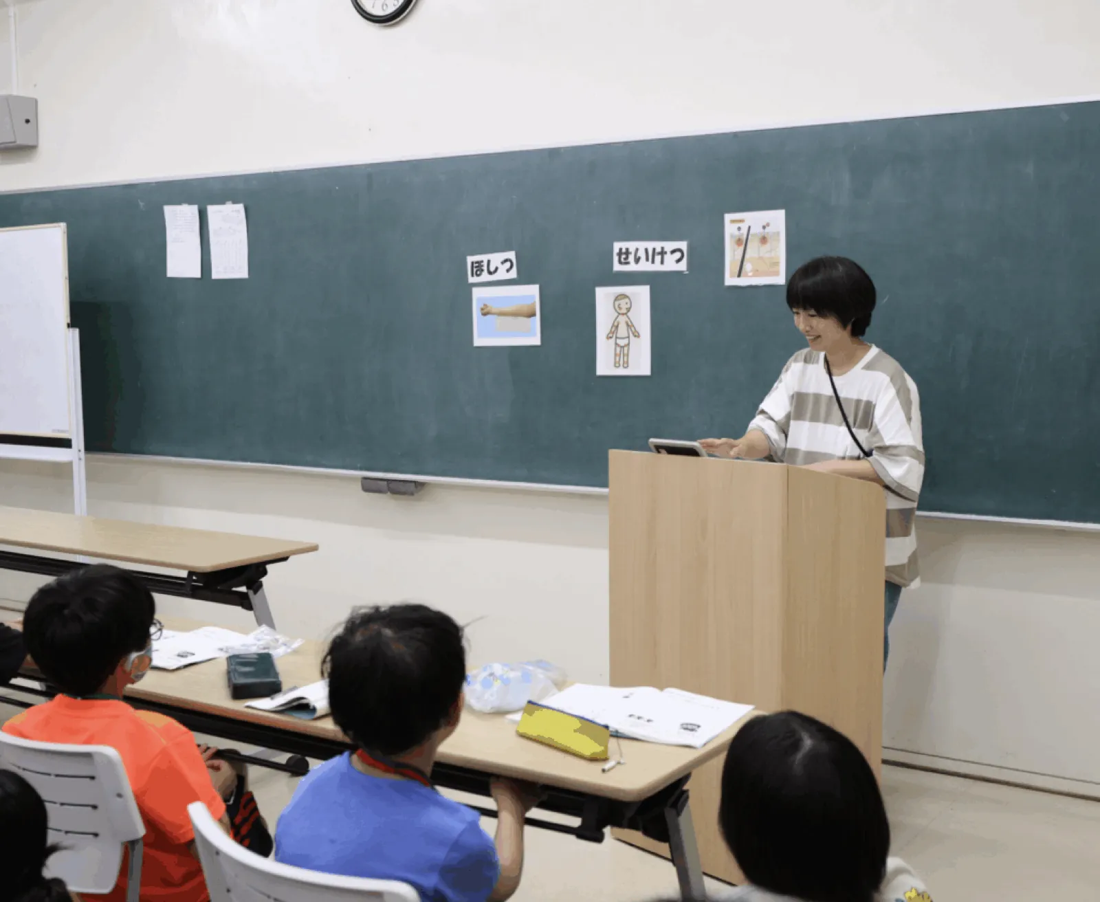 スキンケアの学習会で、黒板に「ほしつ」「せいけつ」の絵カードを貼り、スタッフが演台から話している。